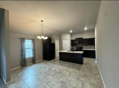 Kitchen with dark cabinets, backsplash, a chandelier, black appliances, and a center island with sink