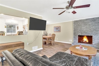 Living area featuring ornamental molding, light wood-style floors, a large fireplace, and a ceiling fan