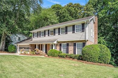 View of front of home with an attached garage, brick siding, concrete driveway, a chimney, and a front lawn