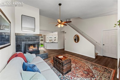Living area featuring wood finished floors, a fireplace, stairs, ceiling fan, and vaulted ceiling