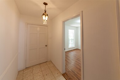 Bright entryway with tile flooring and a classic light fixture. Leads into a room with wood flooring and a large window.