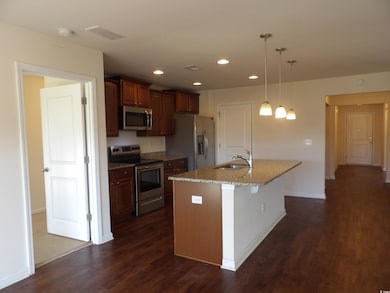 Kitchen with stainless steel appliances, a sink, dark wood-style flooring, an island with sink, and hanging light fixtures