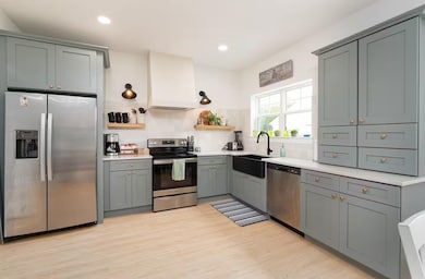 Kitchen featuring stainless steel appliances, open shelves, premium range hood, gray cabinets, and recessed lighting