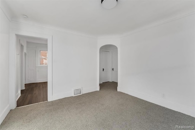 Carpeted spare room featuring arched walkways and crown molding