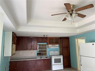 Kitchen with sink, ceiling fan, a raised ceiling, dark brown cabinets, and white appliances