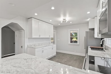 Kitchen featuring stainless steel appliances, recessed lighting, white cabinets, light stone countertops, and arched walkways