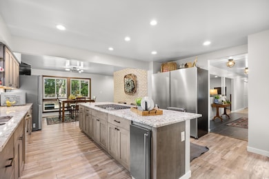 Kitchen featuring appliances with stainless steel finishes, a center island, light wood finished floors, recessed lighting, and light stone countertops