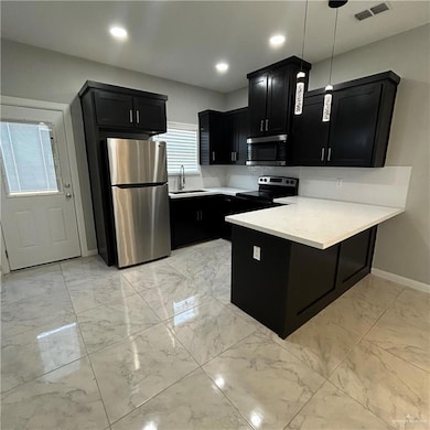 Kitchen featuring dark cabinets, light marble finish floors, appliances with stainless steel finishes, a peninsula, and light countertops