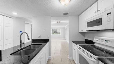 Kitchen featuring white appliances, a sink, dark stone counters, light tile patterned flooring, and white cabinets