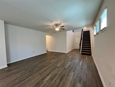 Unfurnished living room with stairway, dark wood-type flooring, and a ceiling fan