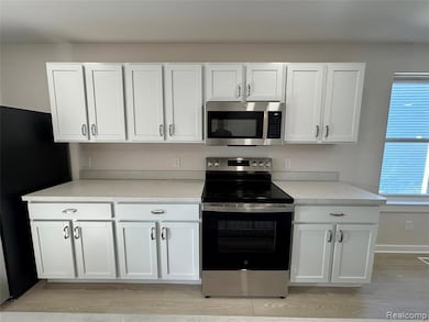 Kitchen featuring appliances with stainless steel finishes, white cabinets, light countertops, and light wood-style floors