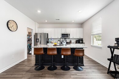 Kitchen featuring appliances with stainless steel finishes, a center island with sink, white cabinetry, a kitchen breakfast bar, and recessed lighting