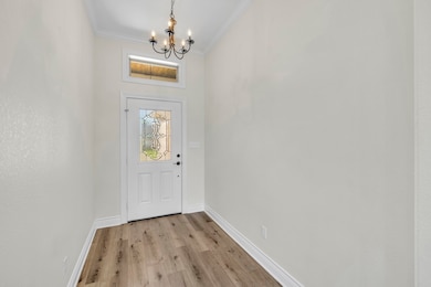 Doorway to outside with a chandelier, crown molding, and light wood-style floors