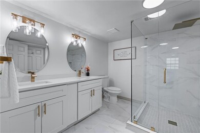 Full bathroom featuring marble finish floors, double vanity, a stall shower, and toilet