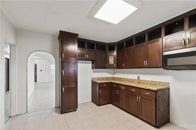 Kitchen with arched walkways, dark brown cabinetry, and light stone counters