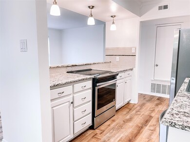 Kitchen with light hardwood / wood-style flooring, tasteful backsplash, stainless steel appliances, white cabinets, and decorative light fixtures