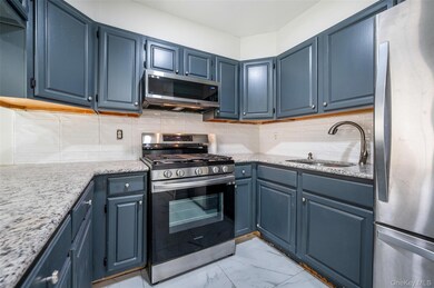 Kitchen featuring appliances with stainless steel finishes, backsplash, light stone counters, and blue cabinetry