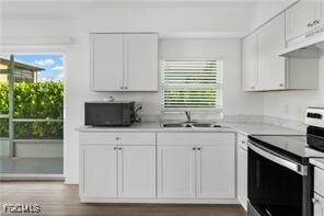 Kitchen featuring stainless steel electric range oven, light countertops, white cabinets, wood finished floors, and black microwave