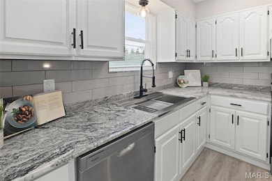 Kitchen featuring white cabinets, stainless steel dishwasher, light stone counters, backsplash, and light wood-style flooring