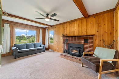 Carpeted living room featuring beamed ceiling, wood walls, a ceiling fan, and a fireplace