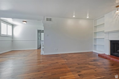 Unfurnished living room featuring dark wood-type flooring, built in shelves, a fireplace with raised hearth, and recessed lighting