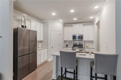 Kitchen featuring appliances with stainless steel finishes, a kitchen bar, white cabinets, light wood-style floors, and crown molding