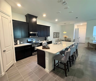 Kitchen featuring appliances with stainless steel finishes, dark cabinets, decorative backsplash, a breakfast bar, and a center island with sink