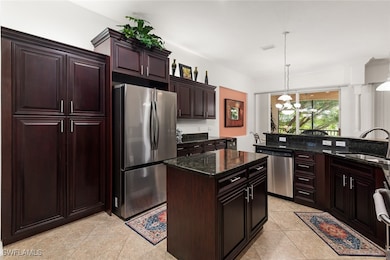Kitchen with stainless steel appliances, a center island, decorative light fixtures, dark stone countertops, and dark brown cabinetry