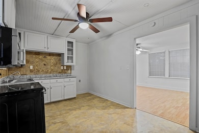 Kitchen featuring white cabinets, black range with electric cooktop, decorative backsplash, glass insert cabinets, and stainless steel microwave
