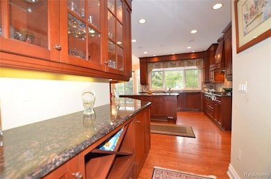 Kitchen with dark stone countertops, light wood-style floors, recessed lighting, glass insert cabinets, and custom range hood