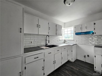 Kitchen featuring dark wood-type flooring, range hood, backsplash, and white cabinets