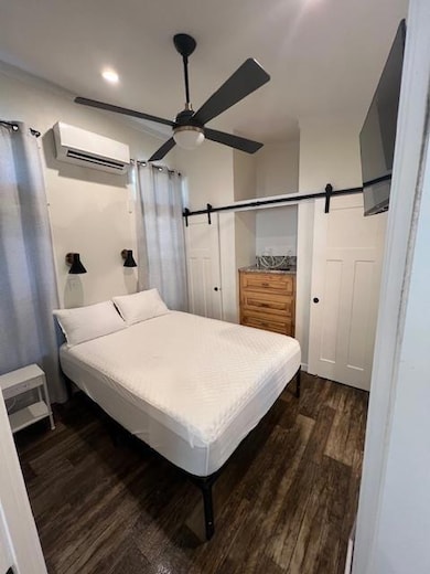 Bedroom featuring a barn door, dark wood-style flooring, ceiling fan, a wall mounted air conditioner, and recessed lighting