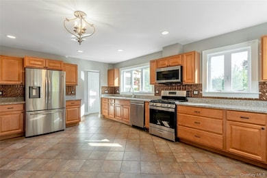 Kitchen featuring backsplash, appliances with stainless steel finishes, light stone countertops, recessed lighting, and hanging light fixtures