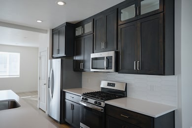 Kitchen featuring stainless steel appliances, glass insert cabinets, light stone counters, decorative backsplash, and recessed lighting