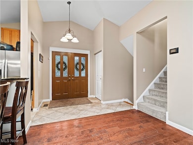 Foyer entrance featuring light wood-style floors, lofted ceiling, stairway, and a chandelier
