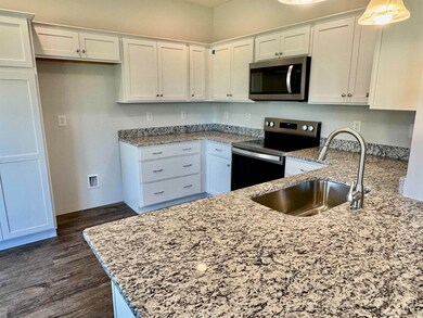 Kitchen featuring stainless steel appliances, light stone counters, white cabinets, and dark wood-style flooring