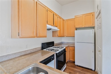 Kitchen featuring white appliances, light brown cabinetry, dark wood finished floors, under cabinet range hood, and light stone countertops