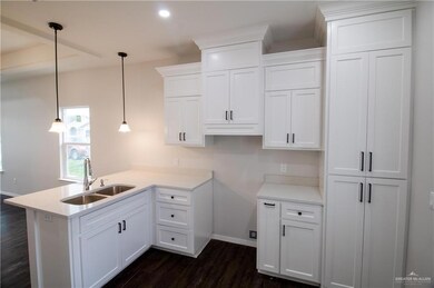 Kitchen featuring sink, white cabinets, pendant lighting, kitchen peninsula, and dark wood-type flooring