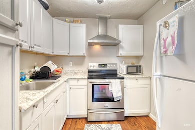 Kitchen featuring freestanding refrigerator, stainless steel electric range oven, wall chimney range hood, dark wood-style flooring, and a textured ceiling