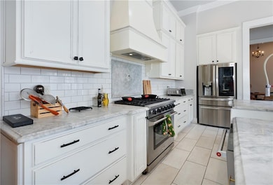 Kitchen featuring stainless steel appliances, premium range hood, crown molding, white cabinet, and stone counters