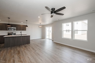 Kitchen with decorative light fixtures, an island with sink, open floor plan, modern cabinets, and dark brown cabinets