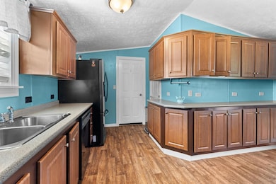 Kitchen with lofted ceiling, light wood-style floors, brown cabinetry, black dishwasher, and a textured ceiling