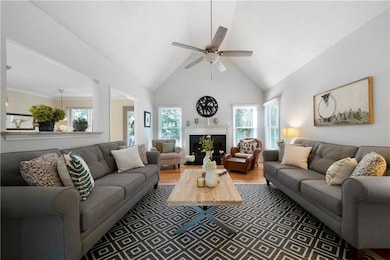 Living room featuring high vaulted ceiling, a ceiling fan, wood finished floors, and a warm lit fireplace