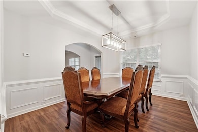Dining space with wainscoting, dark wood-style flooring, a decorative wall, a tray ceiling, and arched walkways