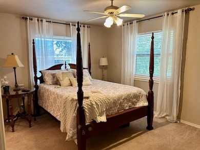 Bedroom featuring multiple windows, light colored carpet, and a ceiling fan