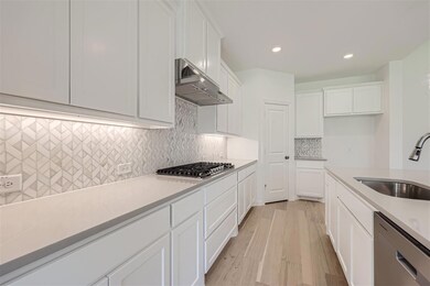Kitchen featuring white cabinetry, tasteful backsplash, light hardwood / wood-style floors, appliances with stainless steel finishes, and sink
