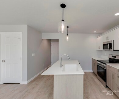 Kitchen with stainless steel appliances, light wood-style floors, hanging light fixtures, recessed lighting, and white cabinets