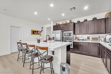 Kitchen featuring dark brown cabinets, light wood-style flooring, a breakfast bar, appliances with stainless steel finishes, and recessed lighting