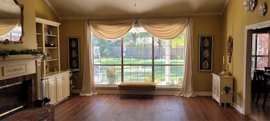 Den with a brick fireplace, dark wood-type flooring, healthy amount of natural light, and crown molding