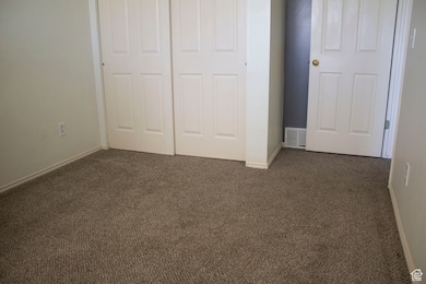 Unfurnished bedroom with visible vents, a closet, dark carpet, and baseboards